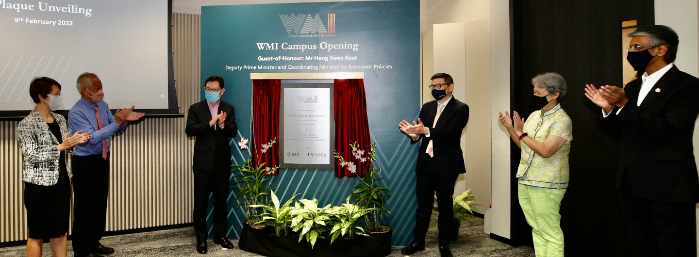 Masked officials applaud WMI Campus Opening plaque unveiling with floral display.